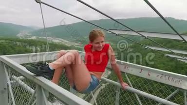 在绿色山谷的背景下，穿着红色T恤的金发<strong>美女</strong>在高山桥上向她的红发<strong>姐姐</strong>摆姿势